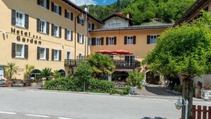 Un hôtel appelé « Hotel Garten », avec un jardin à l’avant, un auvent rouge et une vue sur les montagnes en arrière-plan.