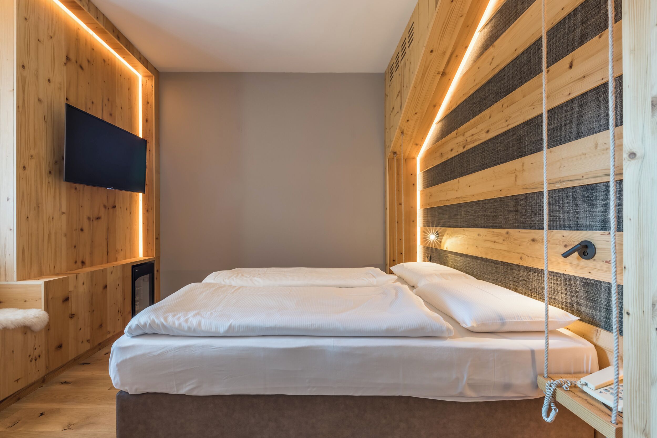 Un dormitorio moderno con una pared de madera, un televisor de pantalla plana, una cama con ropa de cama blanca y una silla colgante.