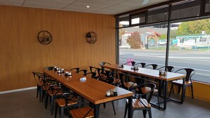 A restaurant with long wooden tables and black chairs, large windows with a view of the street. - 162 Kings of Riccarton Motel (Christchurch)