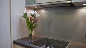 A kitchen with a modern stove, a vase with flowers, and wooden cabinets. - 162 Kings of Riccarton Motel (Christchurch)