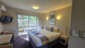 A hotel room with a large bed, a TV mounted on the wall, a window with curtains, and a small table with a chair. - 162 Kings of Riccarton Motel (Christchurch)