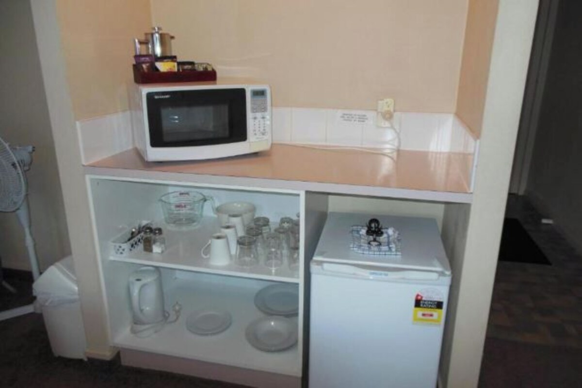 A kitchenette with a microwave, a small refrigerator, and shelves with kitchenware.