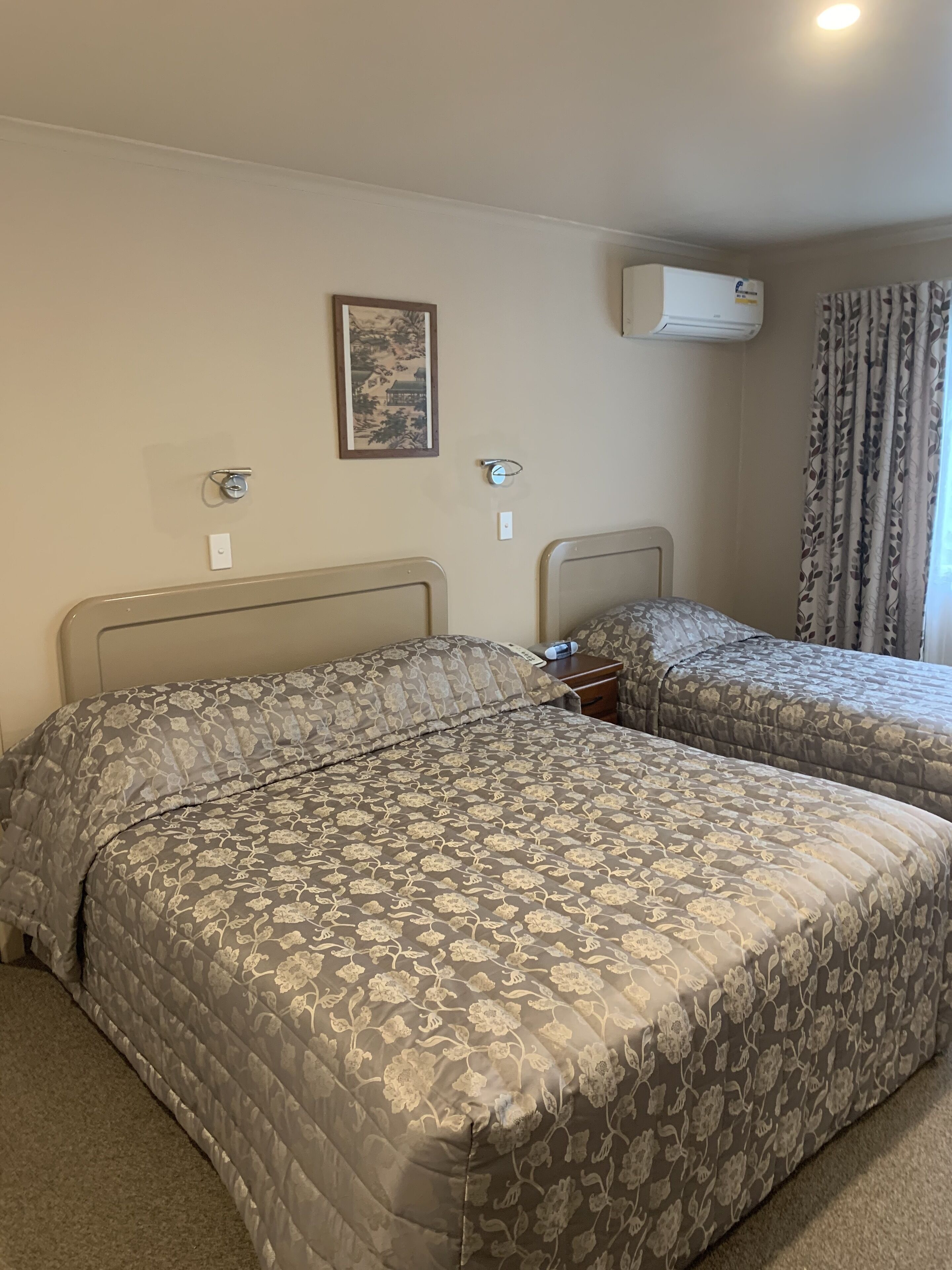 Una camera d'albergo con due letti, una sveglia a parete, un condizionatore d'aria e un quadro incorniciato.