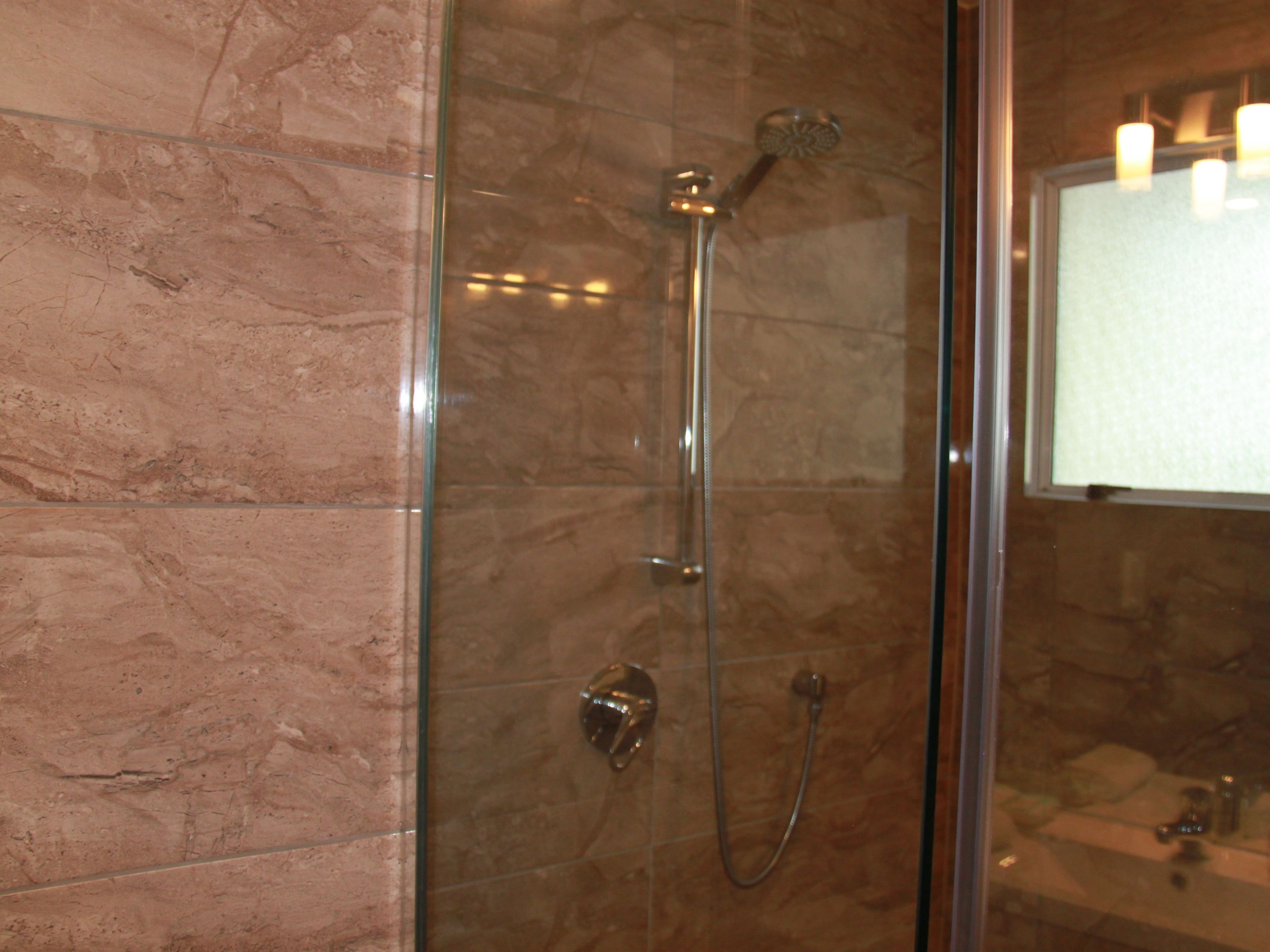 Een douche met glazen wand, een handdouche en een kraan op de muur.