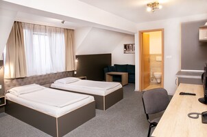 A hotel room with two beds, a desk, a chair, a small table, a sofa, and a bathroom visible through an open door.
