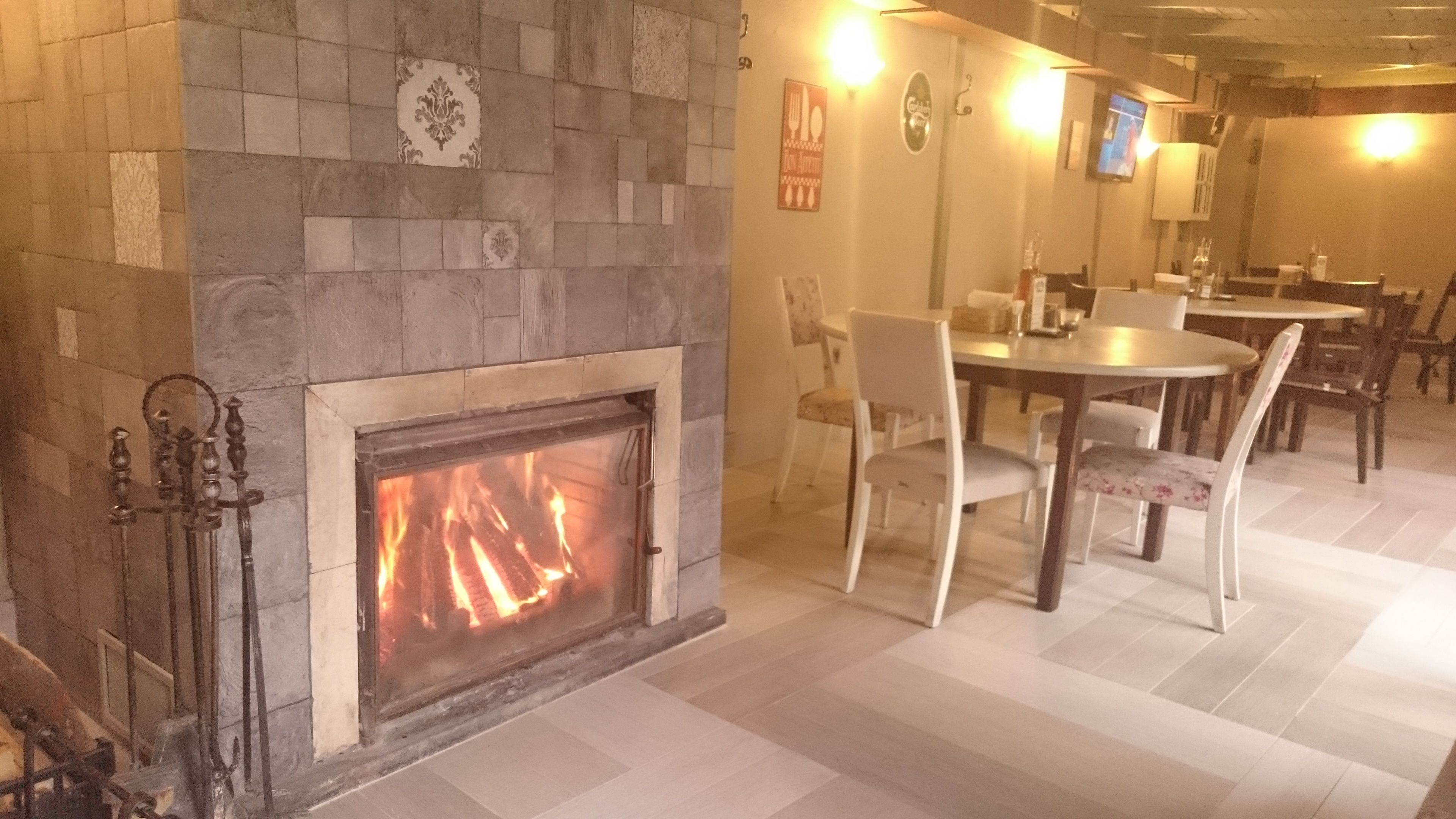 Una chimenea encendida, un área de comedor con sillas y una mesa, y un televisor montado en la pared.
