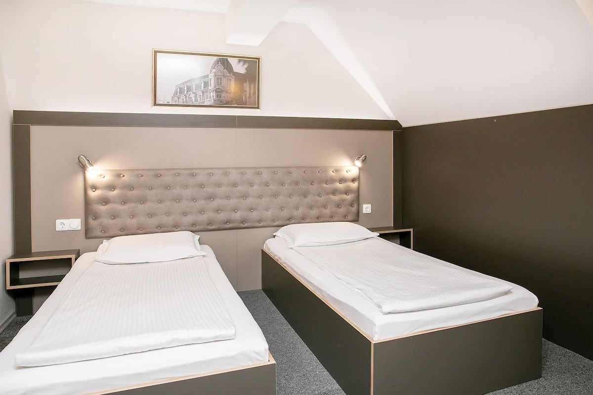 A hotel room with two single beds, a large padded headboard, and a framed picture on the wall.