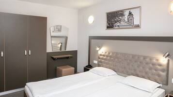 Una habitación de hotel con una cama grande, un armario, una mesita de noche con lámpara, un espejo y un cuadro en la pared.