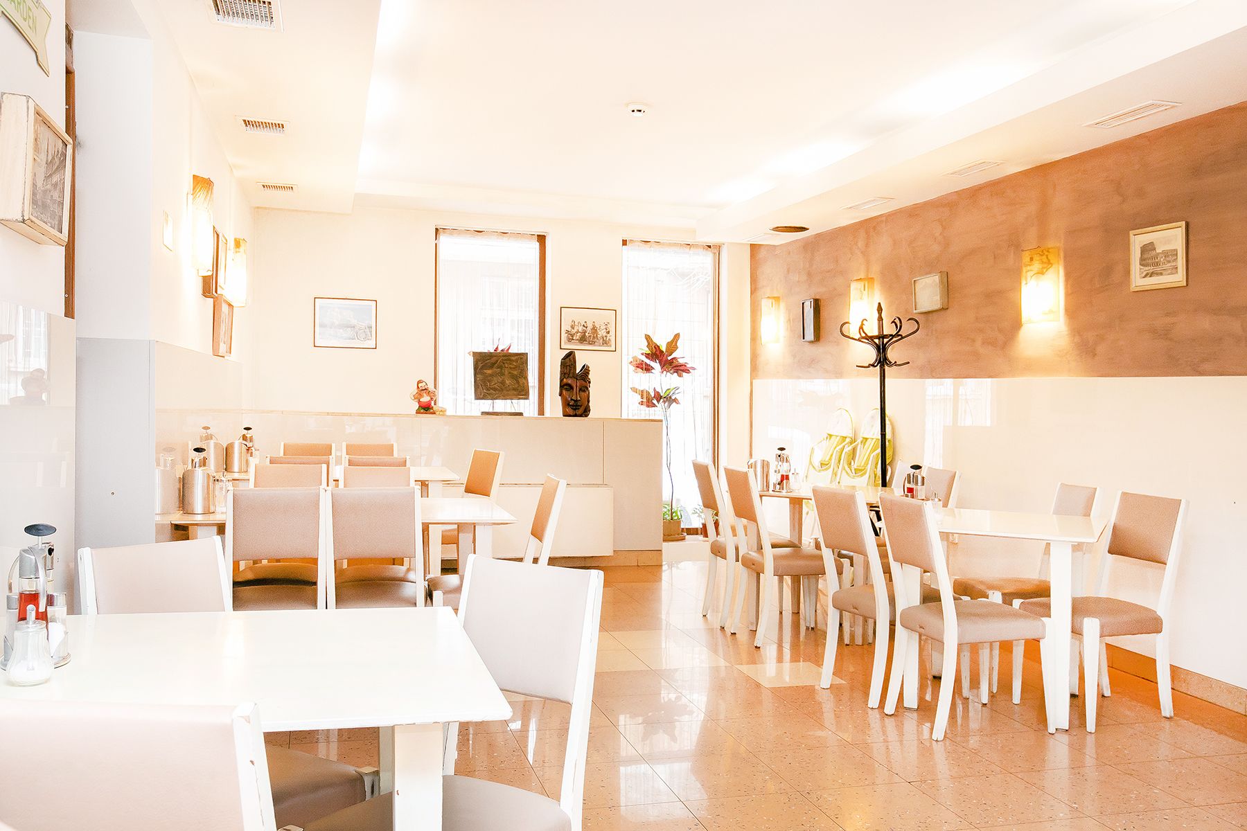 Un restaurante con mesas y sillas blancas, una pared de acento de madera y obras de arte enmarcadas en las paredes.