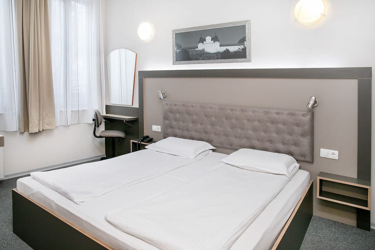A hotel room with a large bed, a desk, a chair, a mirror, and a picture on the wall.