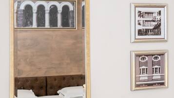A hotel room with a large mirror reflecting a bed and a wall with three framed pictures.