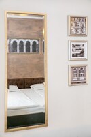 A hotel room with a large mirror reflecting a bed and a wall with three framed pictures.