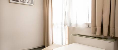 A small, minimalist room with a white desk, a radiator, and a window with sheer curtains.
