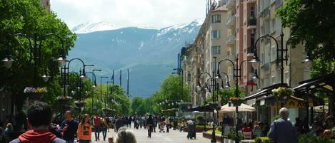 Una calle animada con gente caminando, cafés y edificios con balcones.