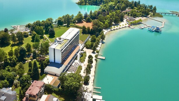 Vue aérienne d’une zone côtière avec un bâtiment moderne, un quai et une petite île couverte d’arbres.