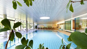 Une piscine intérieure dotée d’un sol carrelé, de chaises longues et d’un plafond orné d’un motif linéaire.