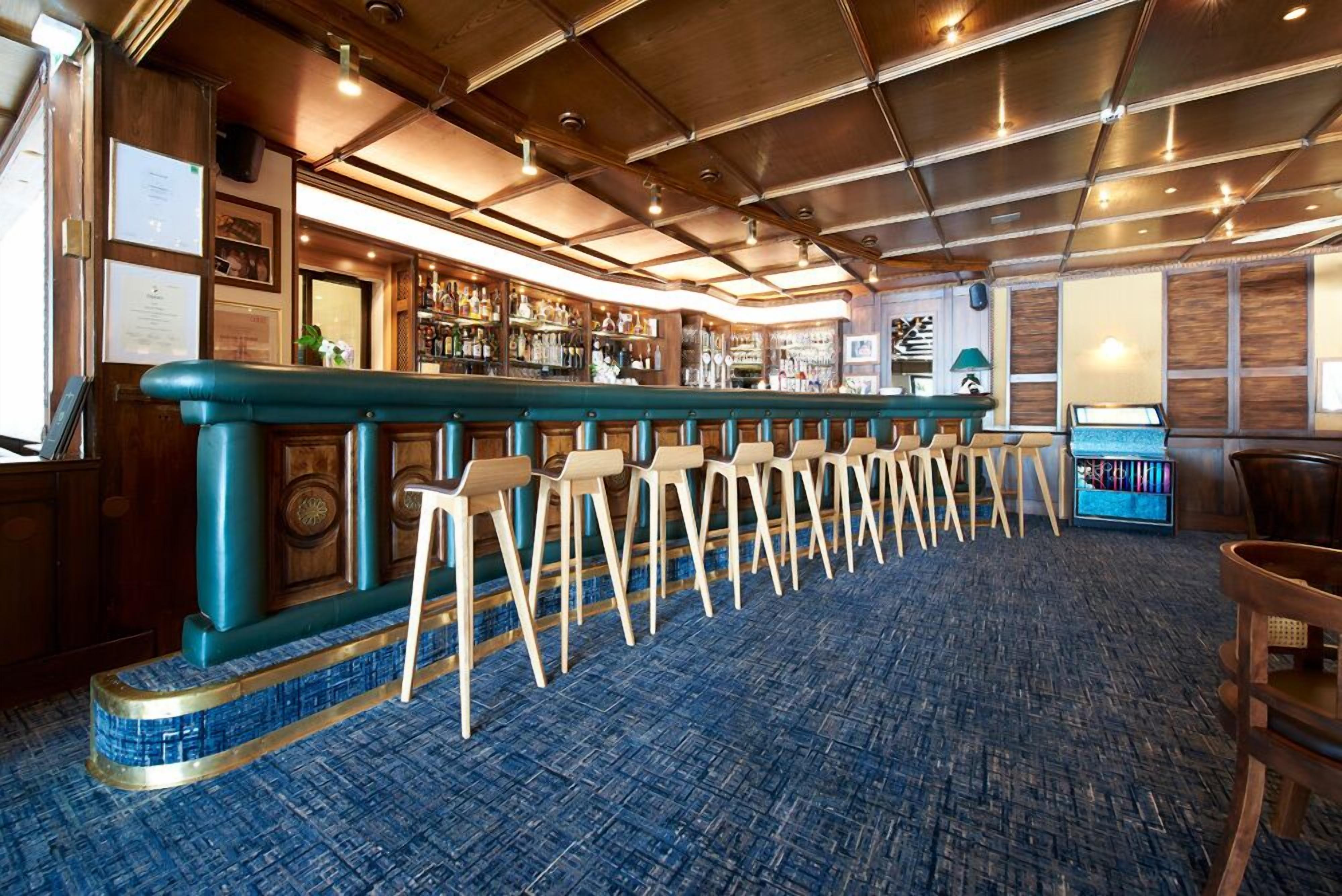 Een bar met een lange toonbank, barkrukken en een vloerkleed.