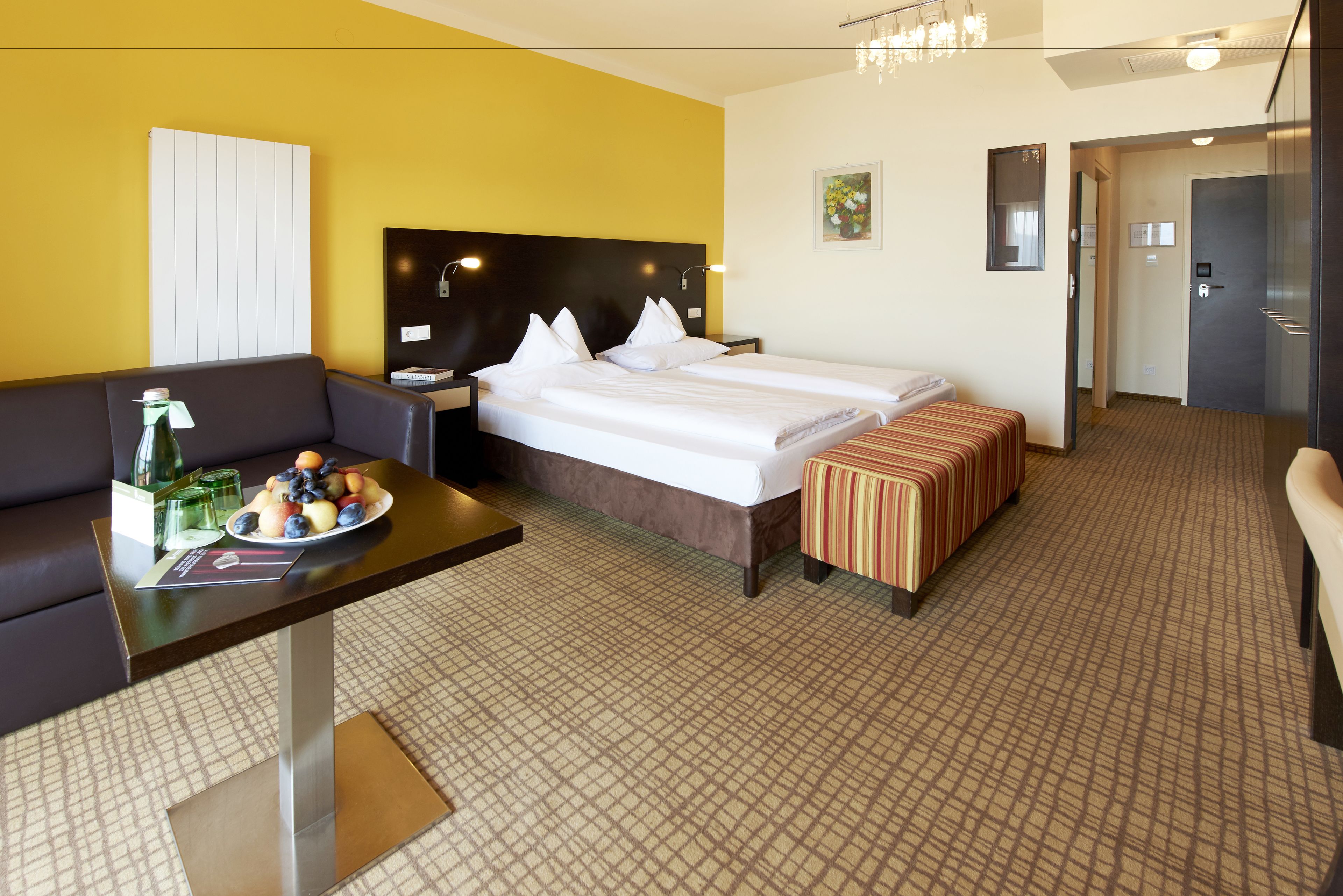 Habitación de hotel con cama, mesita de noche con fruta, un sofá y una pequeña mesa.