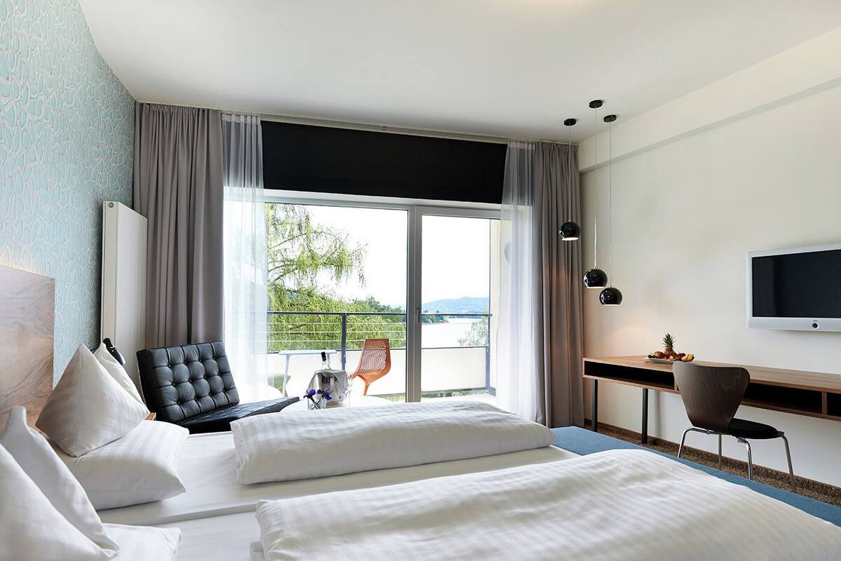 Habitación de hotel con cama, escritorio, silla, televisor y balcón con vistas.