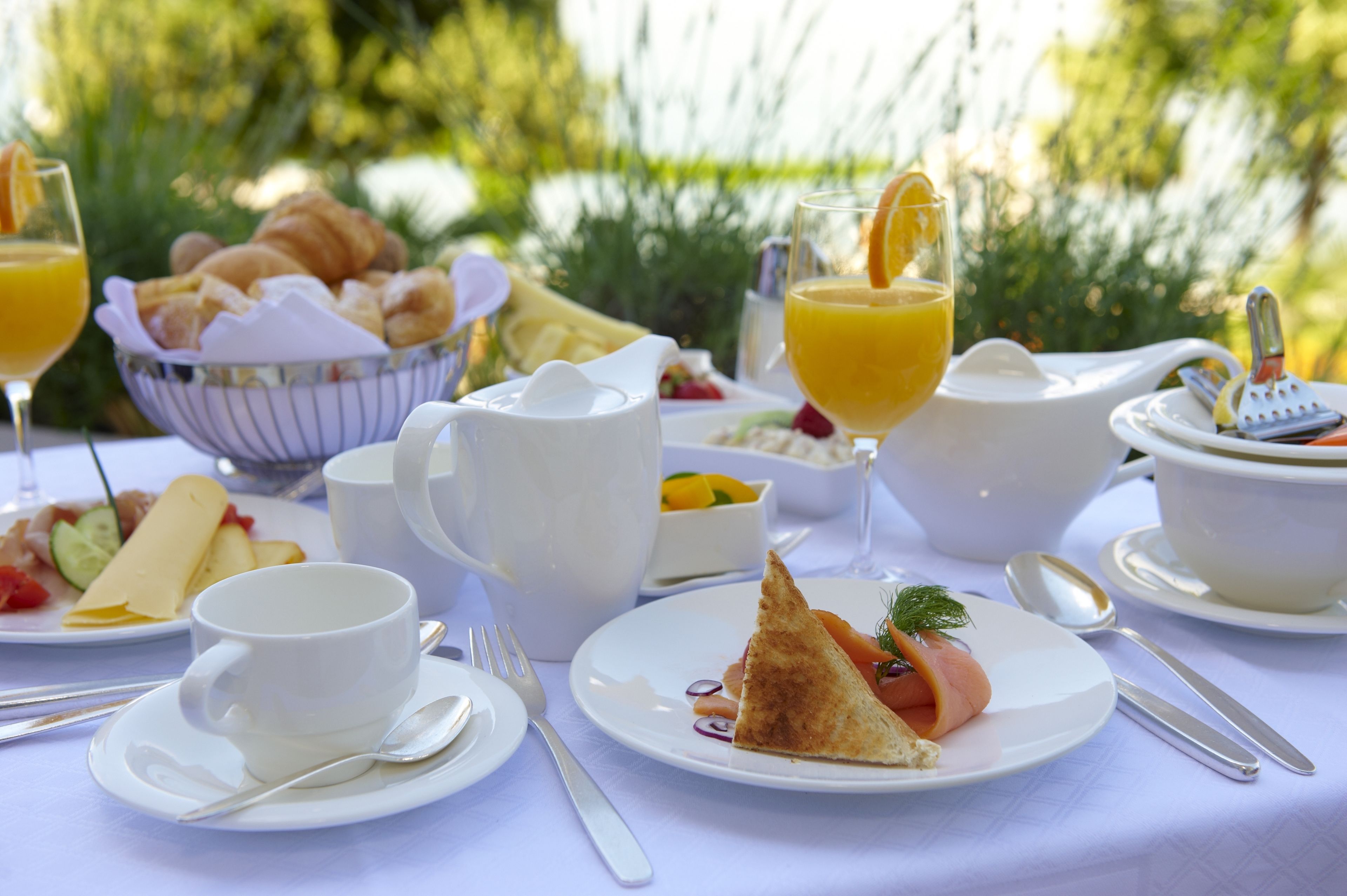 Una mesa de desayuno con platos de comida, una cesta de croissants, una jarra de jugo de naranja y una taza de café.