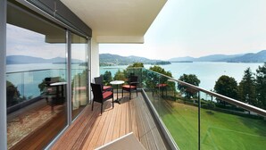 Un balcon avec vue sur un lac et des montagnes, aménagé avec des chaises et une table.