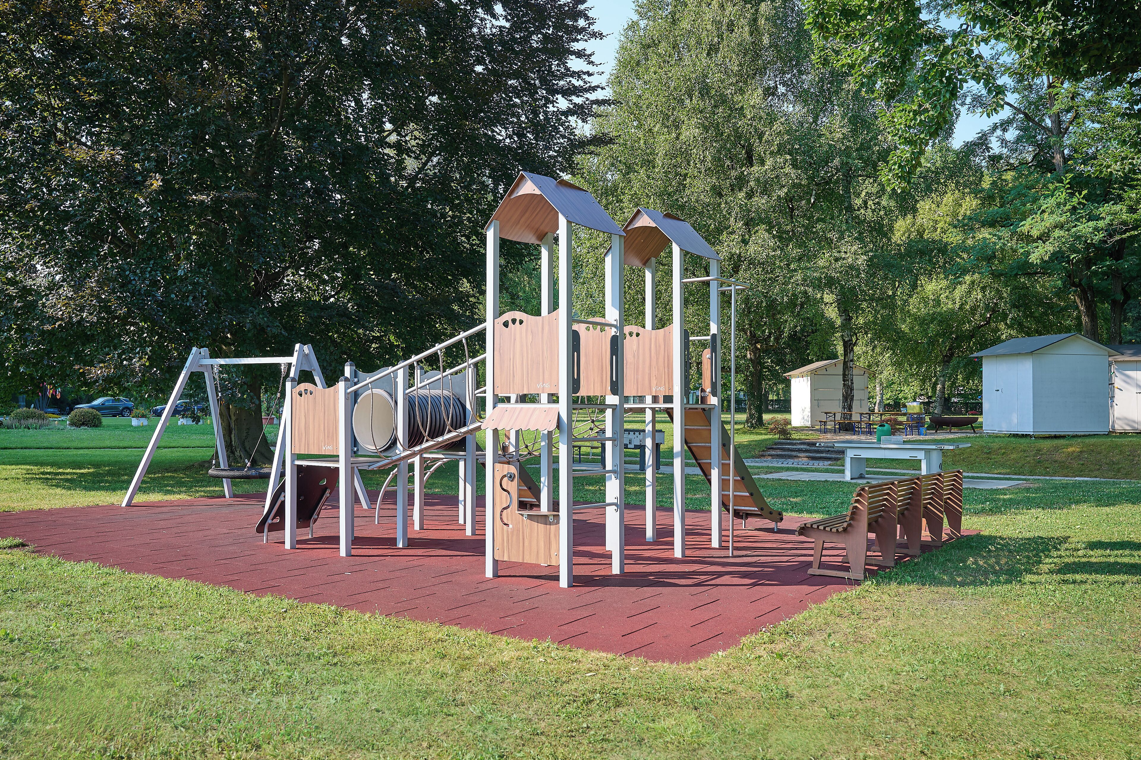 Ein Spielplatz mit einer hölzernen Kletterkonstruktion, Schaukeln und einer Rutsche.