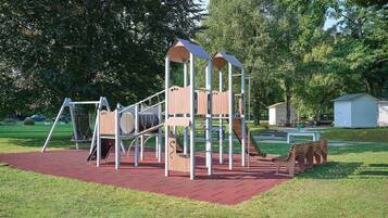 Ein Spielplatz mit einer hölzernen Kletterkonstruktion, Schaukeln und einer Rutsche.