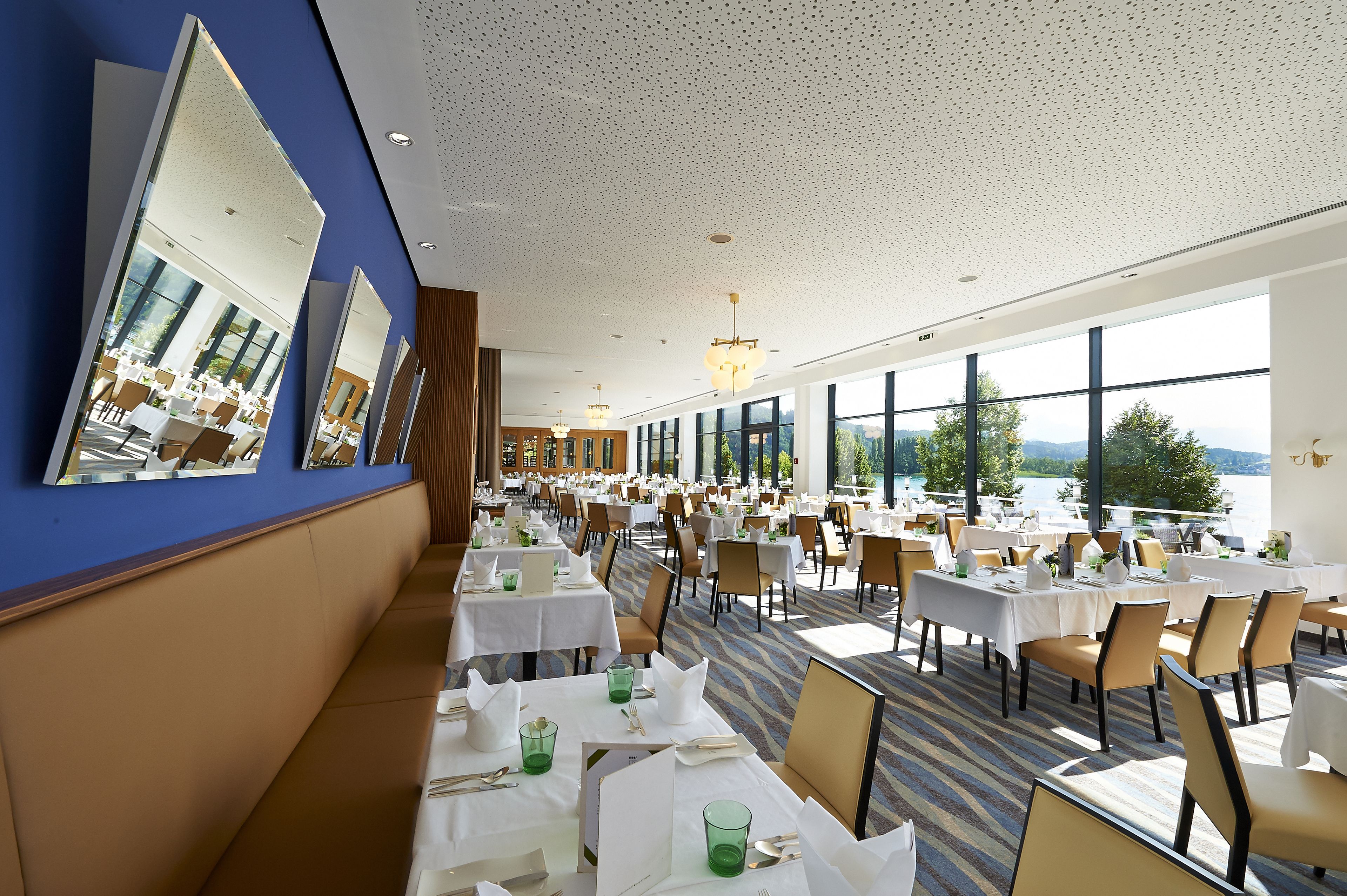 Un comedor amplio con varias mesas y sillas, ventanas grandes que ofrecen vistas al exterior y un techo con diseño moteado.