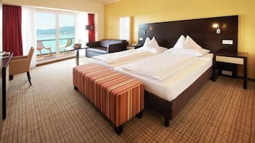 A hotel room with two beds, a desk, a chair, a bench, and a view of the sea.