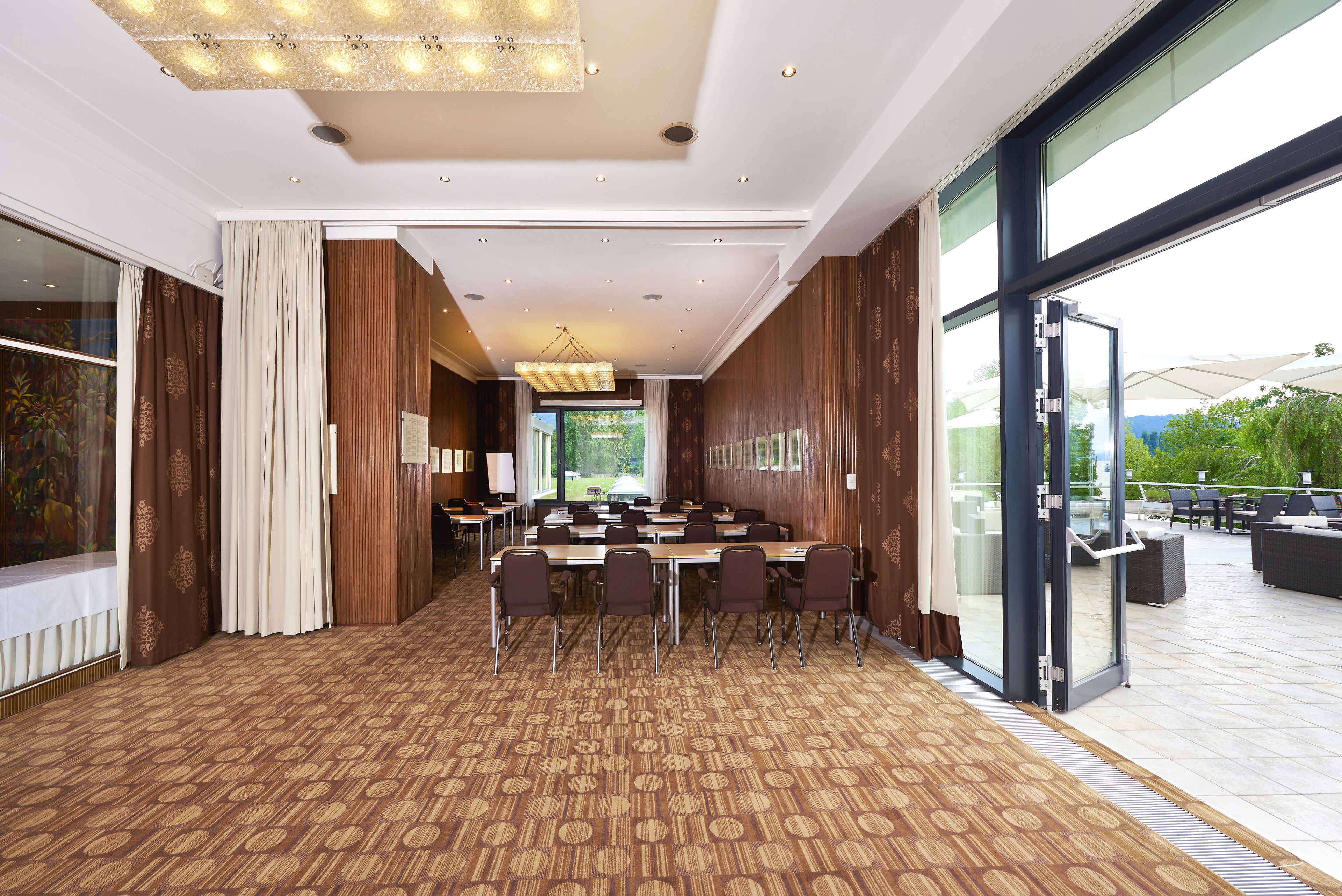 Uma sala de conferências com carpete estampado, um lustre grande e vista para o exterior através de amplas janelas.