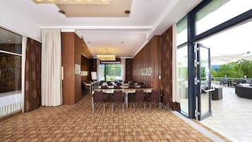 Uma sala de conferências com carpete estampado, um lustre grande e vista para o exterior através de amplas janelas.
