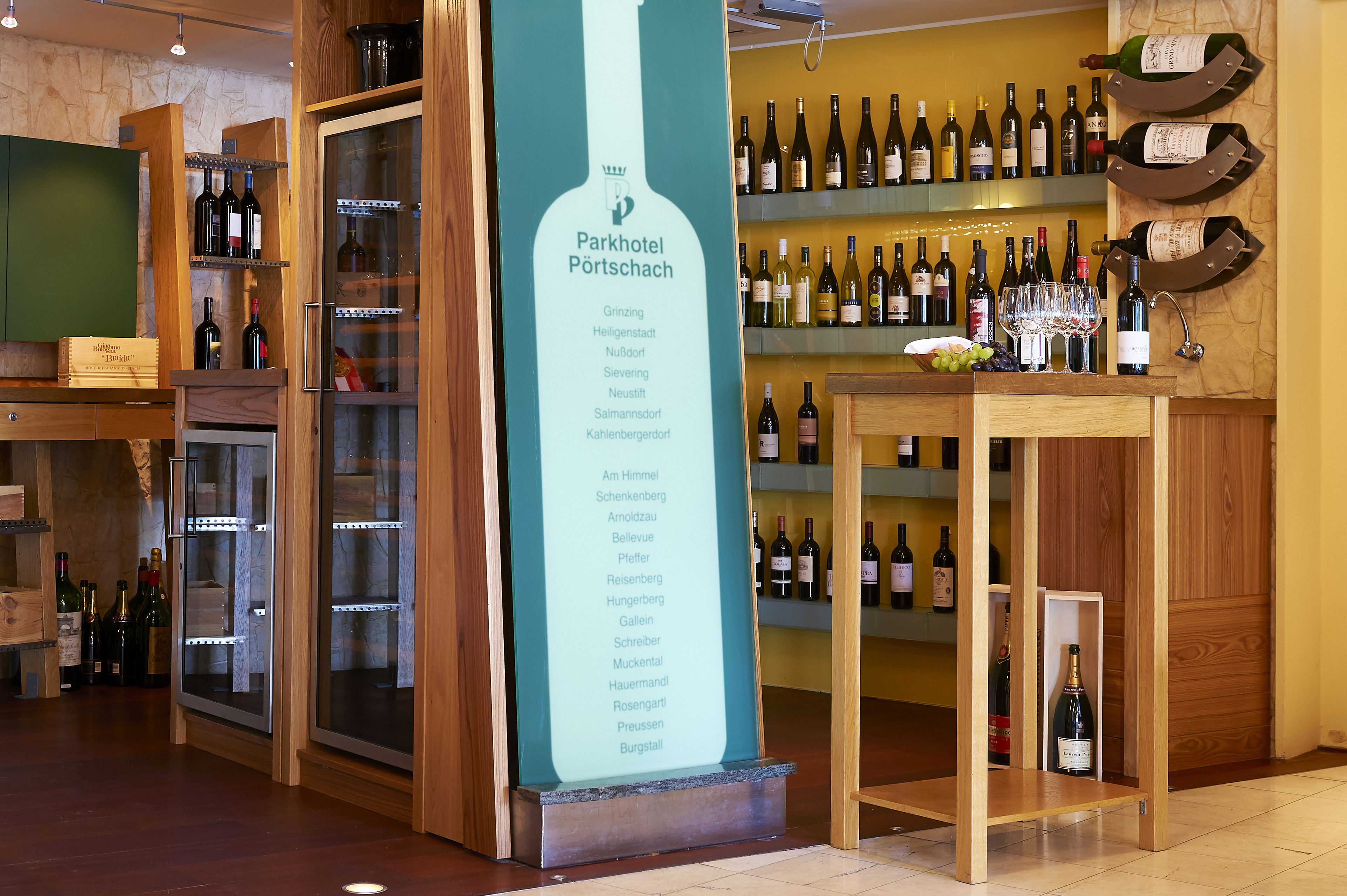 Una bodega con una variedad de botellas de vino en estantes y un cartel grande que enumera diferentes regiones vinícolas.