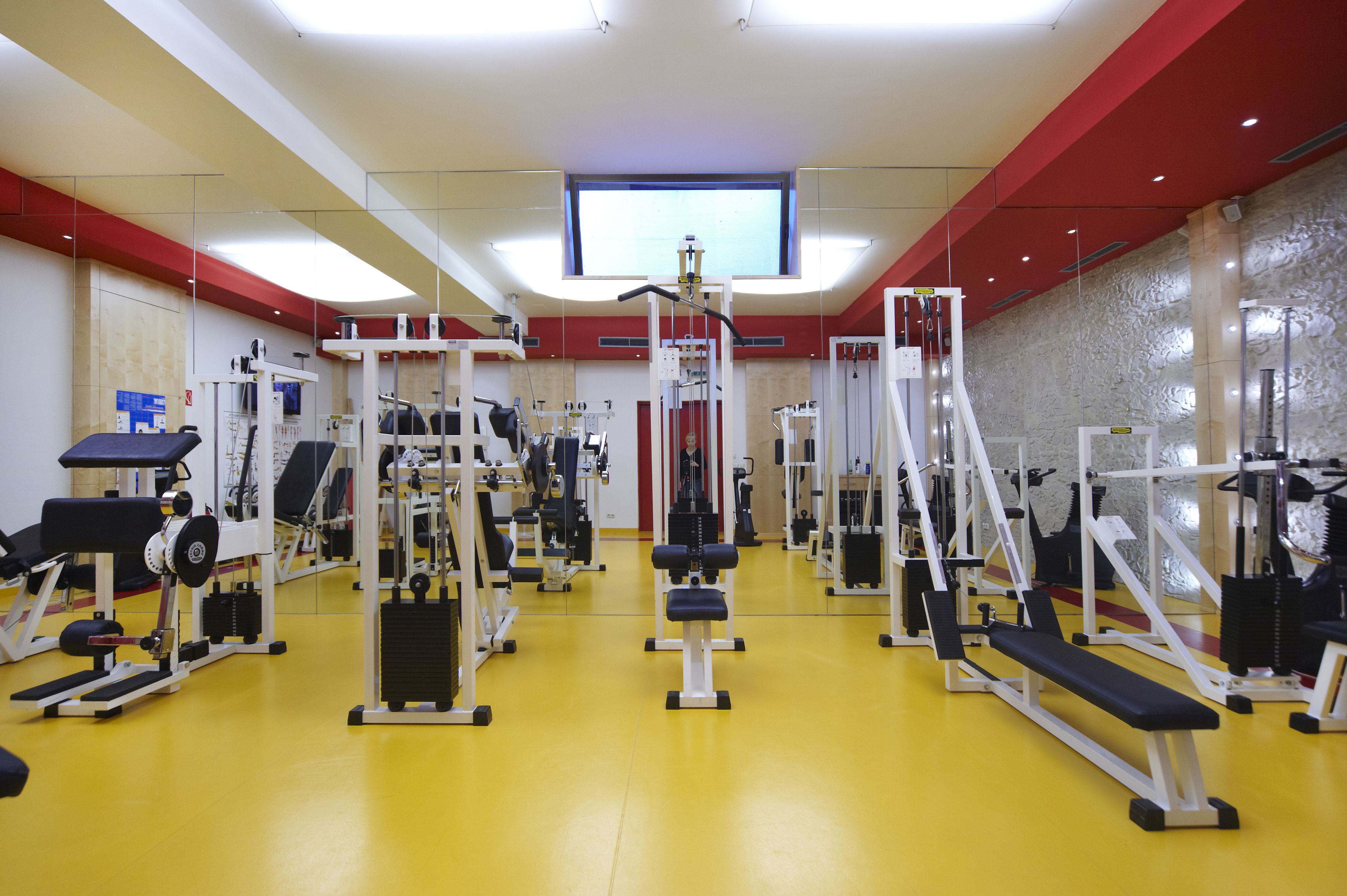 A gym with various exercise equipment, a large mirror, and a television screen on the wall.