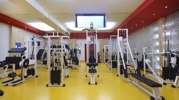 Une salle de sport équipée de divers appareils d’exercice, dotée d’un grand miroir et d’un écran de télévision fixé au mur.