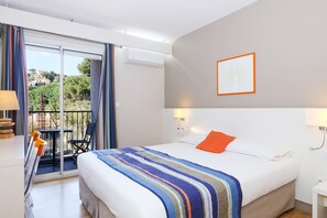 Habitación de hotel con cama, mesita de noche, lámpara, silla y balcón con mesa y sillas.