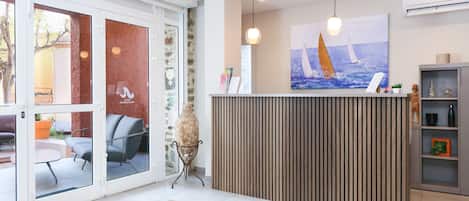 A reception area with a wooden reception desk, a large painting of sailboats, a potted plant, and a grey shelving unit.