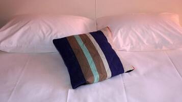 Una cama con sábanas blancas y una almohada decorativa a rayas.