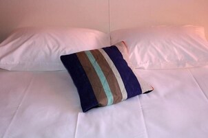 Una cama con sábanas blancas y una almohada decorativa a rayas.