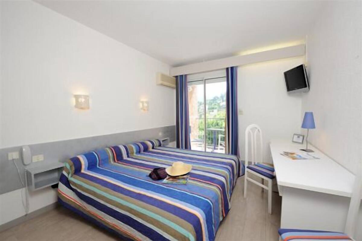 A hotel room with a bed, a desk, a chair, a TV, and a balcony with a view.