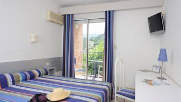 Habitación de hotel con cama, escritorio, televisión y vistas a un balcón con barandilla.