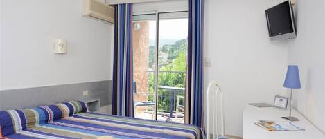 A hotel room with a bed, a desk, a television, and a view of a balcony with a railing.