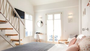 A bedroom with a bed, a chair, a desk, a mirror, and a staircase.