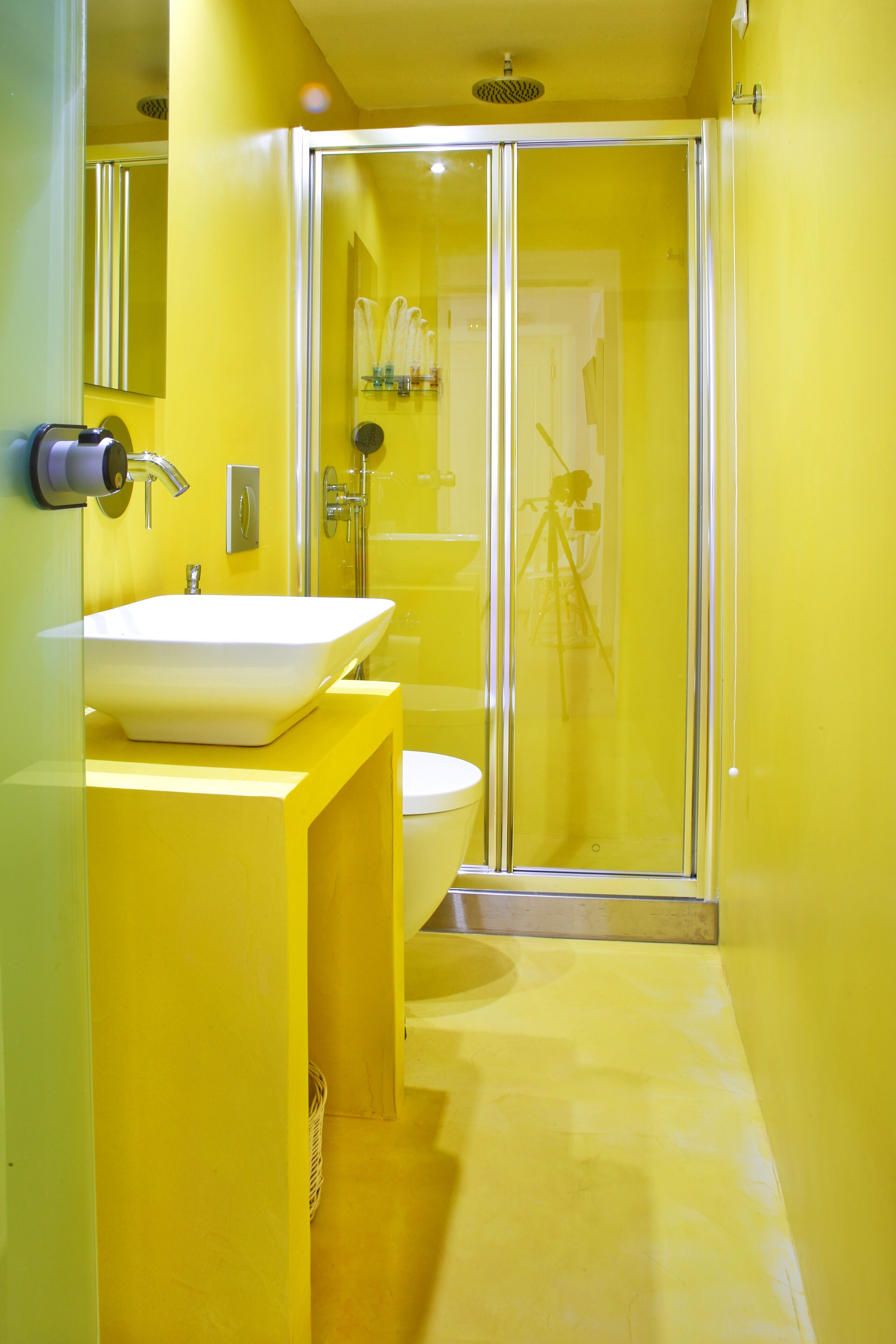 Casa de banho moderna com esquema de cores amarelo, apresentando uma cabine de duche envidraçada, uma sanita branca e uma pia.