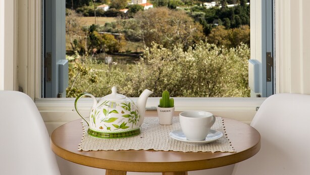 A window with a view of a hilly landscape, a white teapot, a white cup, and a small potted plant on a table.