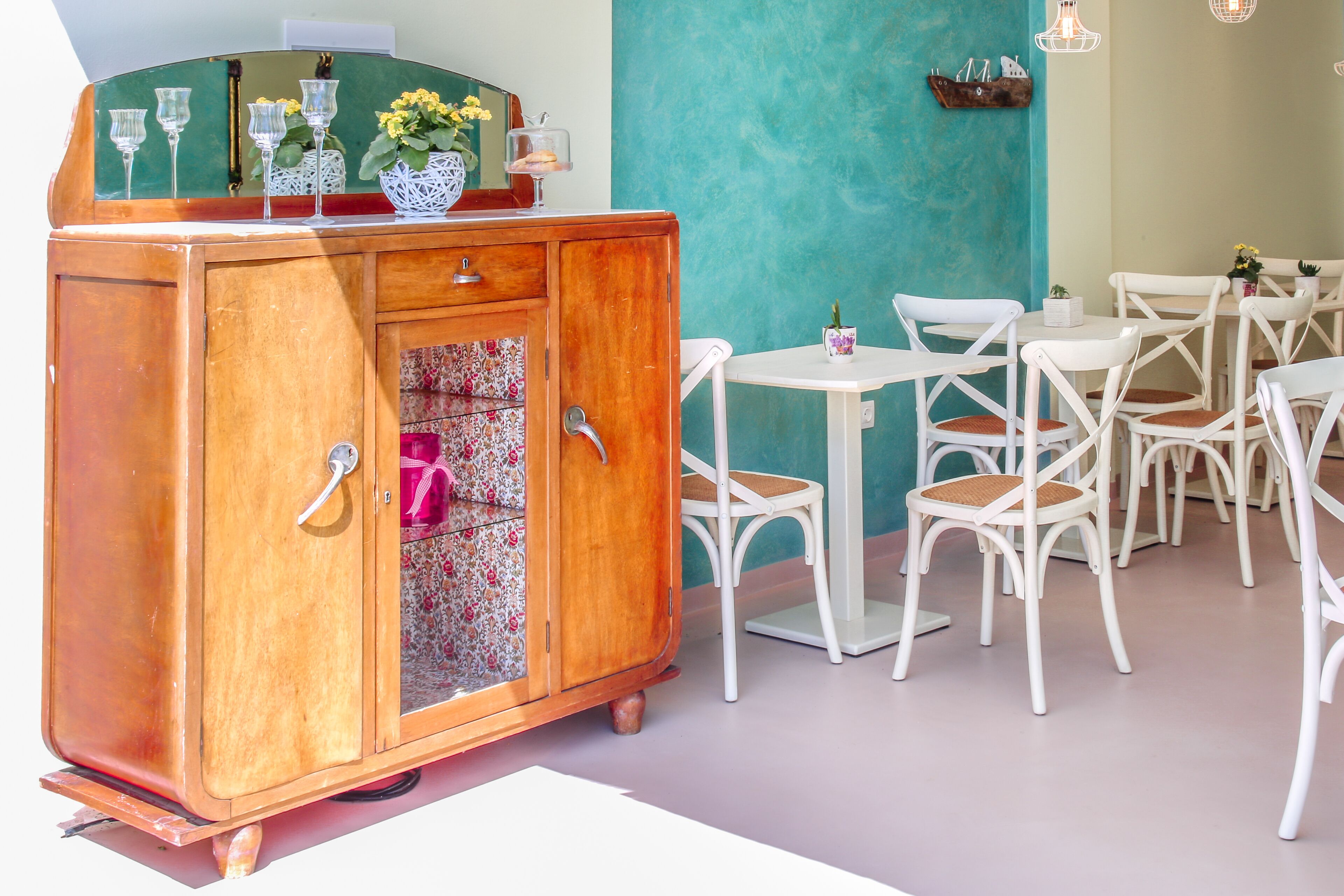 A dining area with a wooden cabinet, white chairs, and a teal wall.
