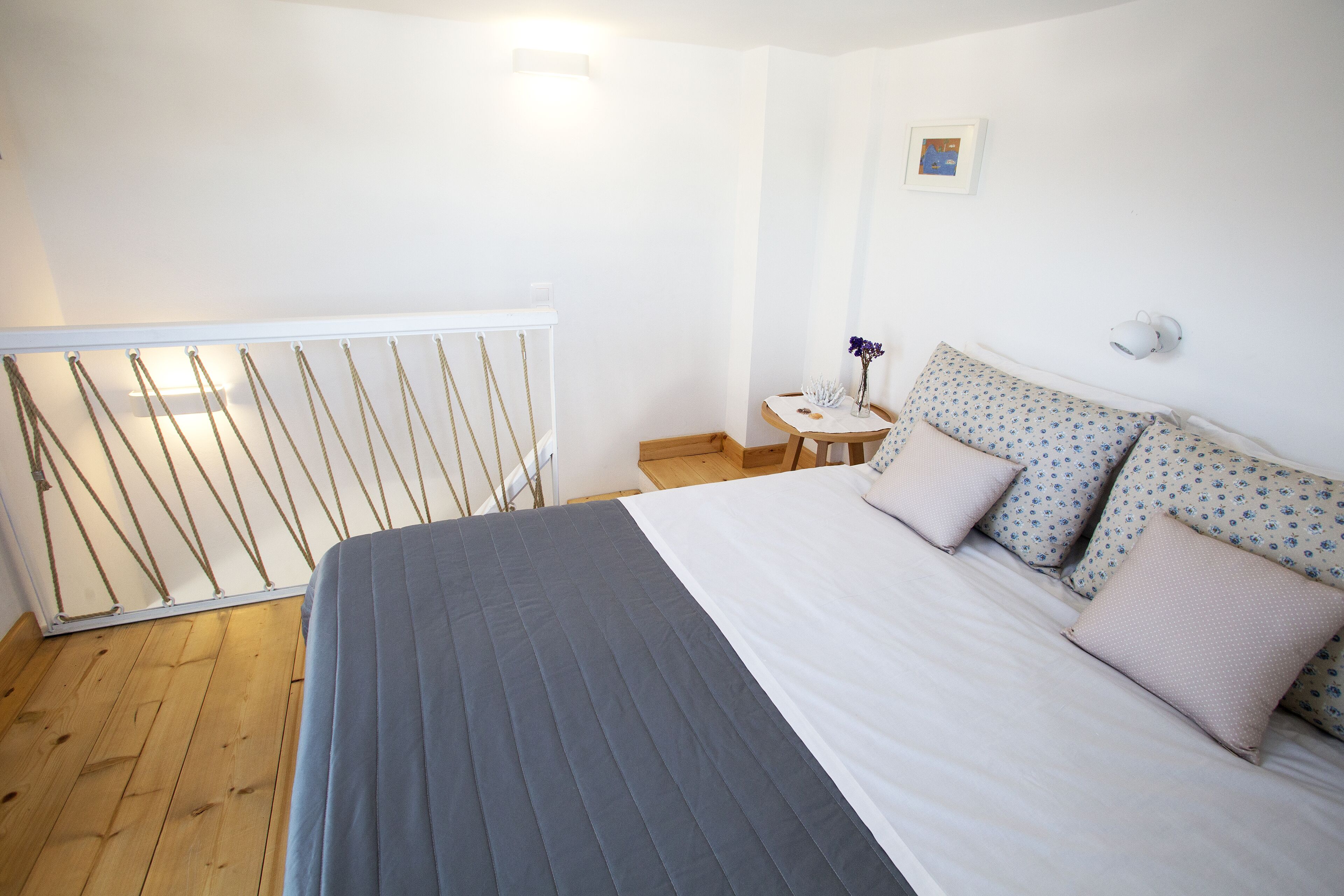 A bedroom with a bed, a small table with a vase, and a wall-mounted lamp.