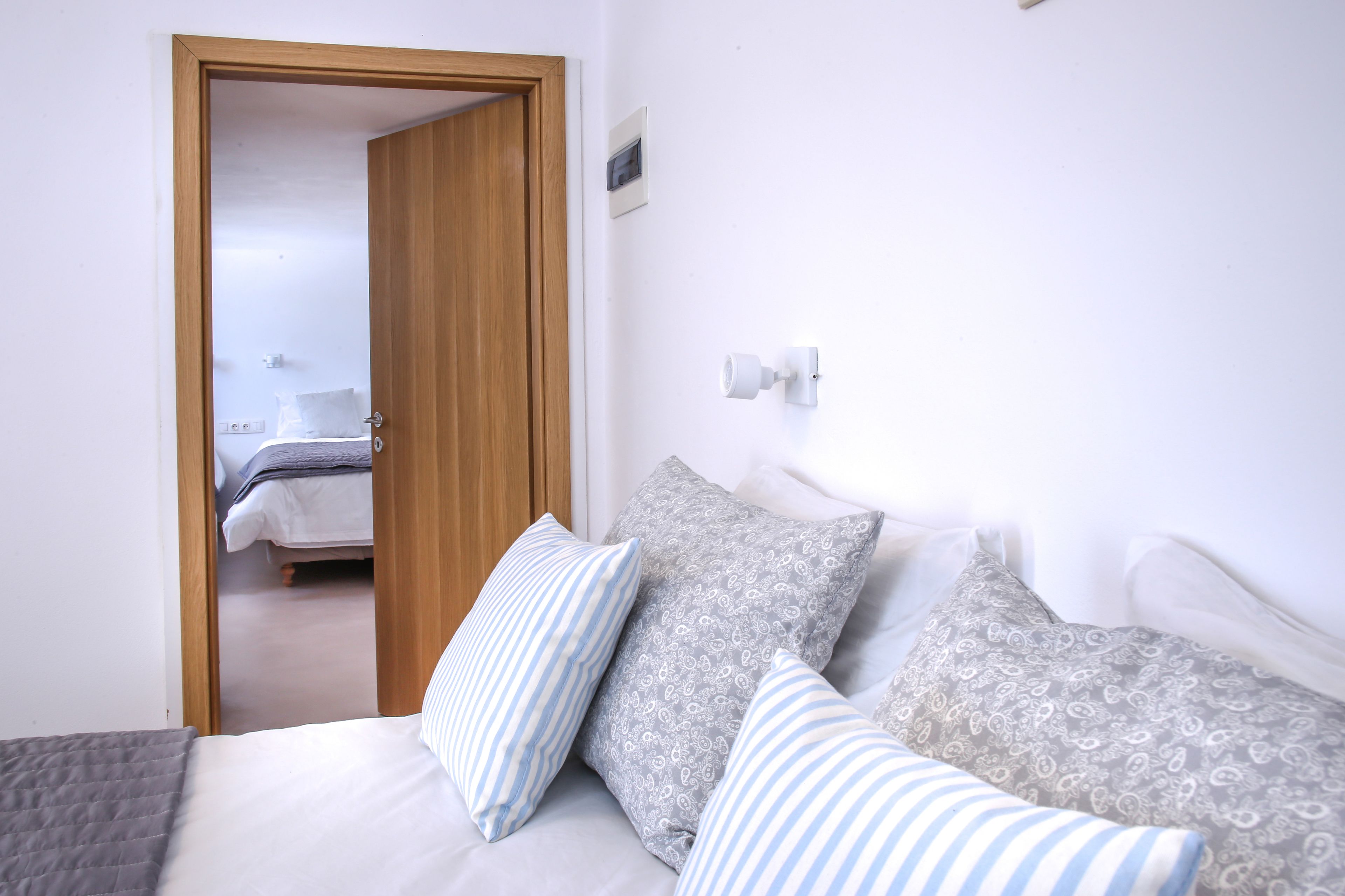A bedroom with a wooden door, a bed with patterned pillows, and a white wall with a light switch.