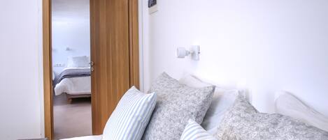 A bedroom with a wooden door, a bed with patterned pillows, and a white wall with a light switch.