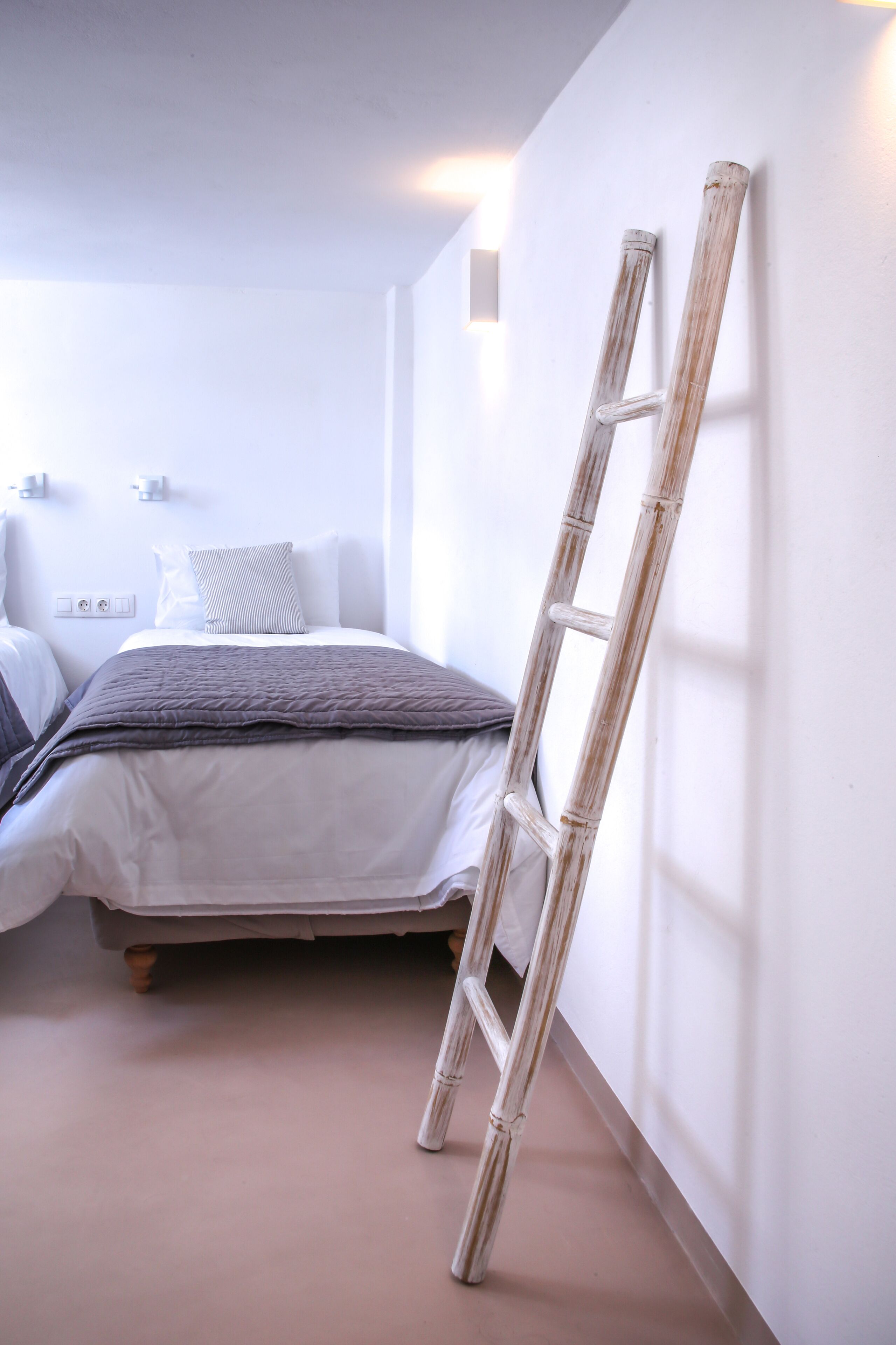 A bedroom with a bed, a ladder leaning against the wall, and a bedside table with a lamp.