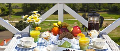A breakfast table with a variety of food items and a coffee maker on a balcony overlooking a scenic landscape.